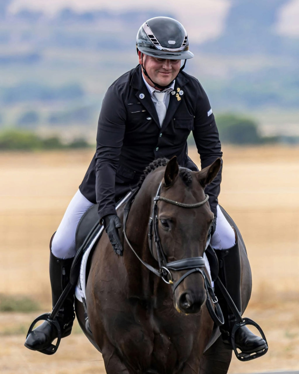 Ryan Fletcher patting his horse in a shiny black equestrian horse riding helmet