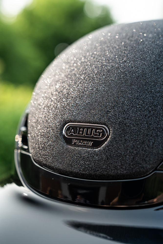 Close-up of a black equestrian horse riding helmet with 'ABUS' branding on a blurred green background