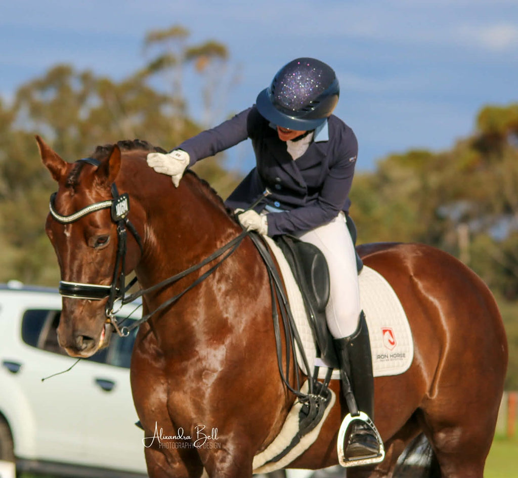 Rider in a navy blue shiny nightsky equestrian horse riding helmet pats her chestnut horse at the completion of a dressage test